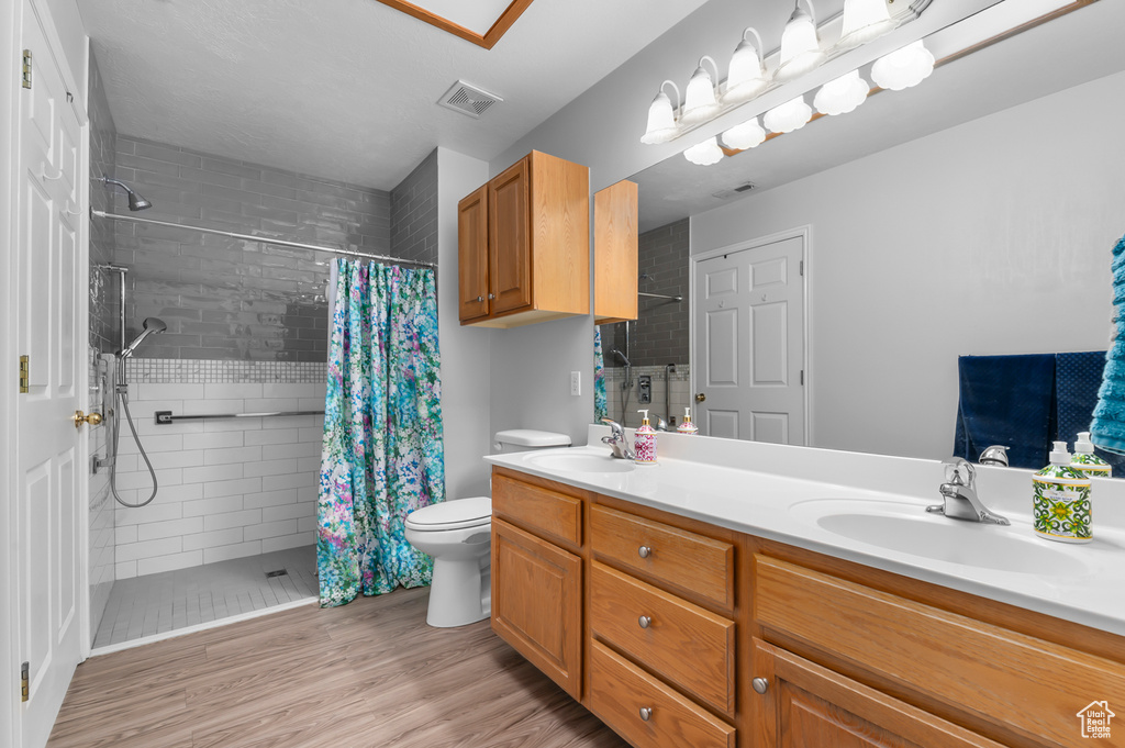 Full bathroom featuring a tile shower, wood finished floors, double vanity, and toilet