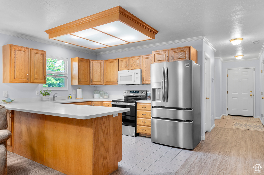 Kitchen featuring appliances with stainless steel finishes, crown molding, a peninsula, light countertops, and light tile patterned floors
