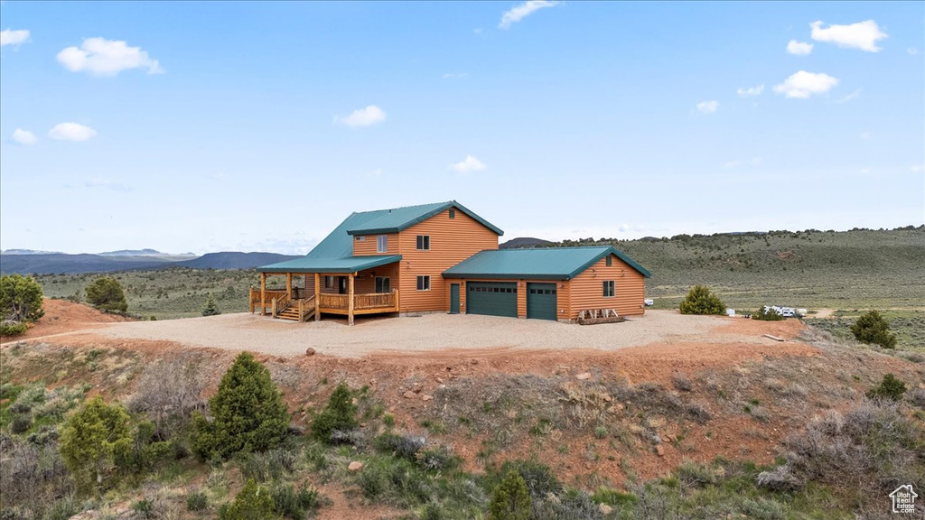 Rear view of house featuring an attached garage, log veneer siding, driveway, metal roof, and a mountain view