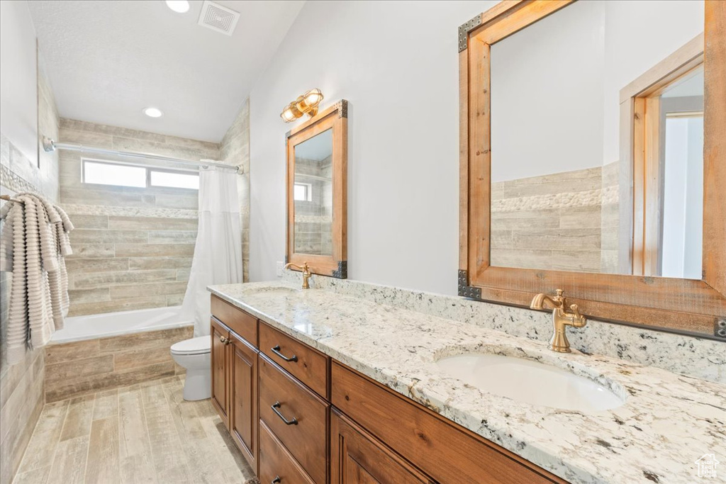 Bathroom featuring wood finished floors, toilet, tiled shower / bath, double vanity, and recessed lighting