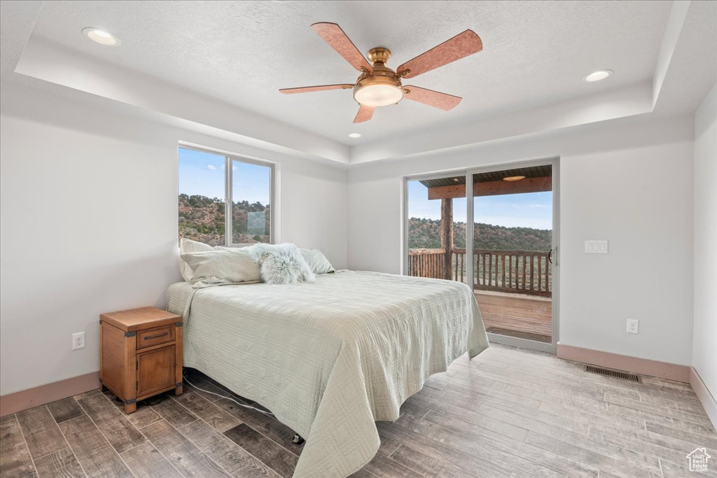 Bedroom featuring a tray ceiling, access to exterior, multiple windows, wood finished floors, and recessed lighting
