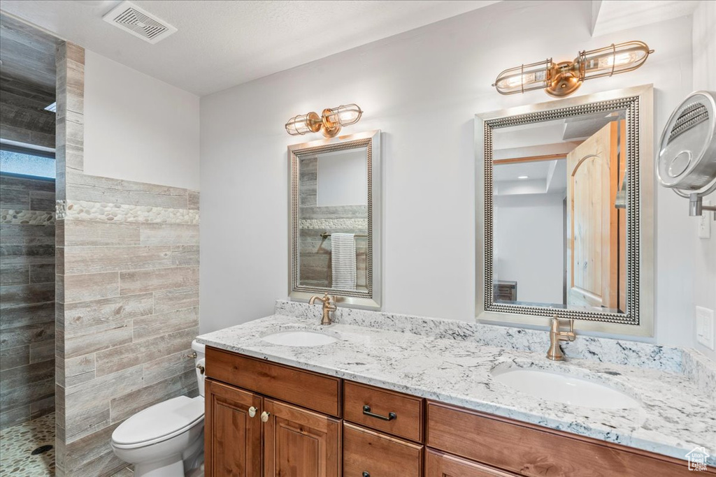 Bathroom with toilet, tiled shower, and double vanity