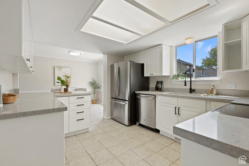 Kitchen featuring stainless steel appliances, a sink, light tile patterned floors, white cabinetry, and a peninsula