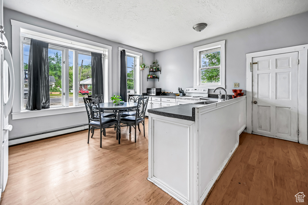 Kitchen featuring white electric stove, a baseboard radiator, a peninsula, a textured ceiling, and dark countertops