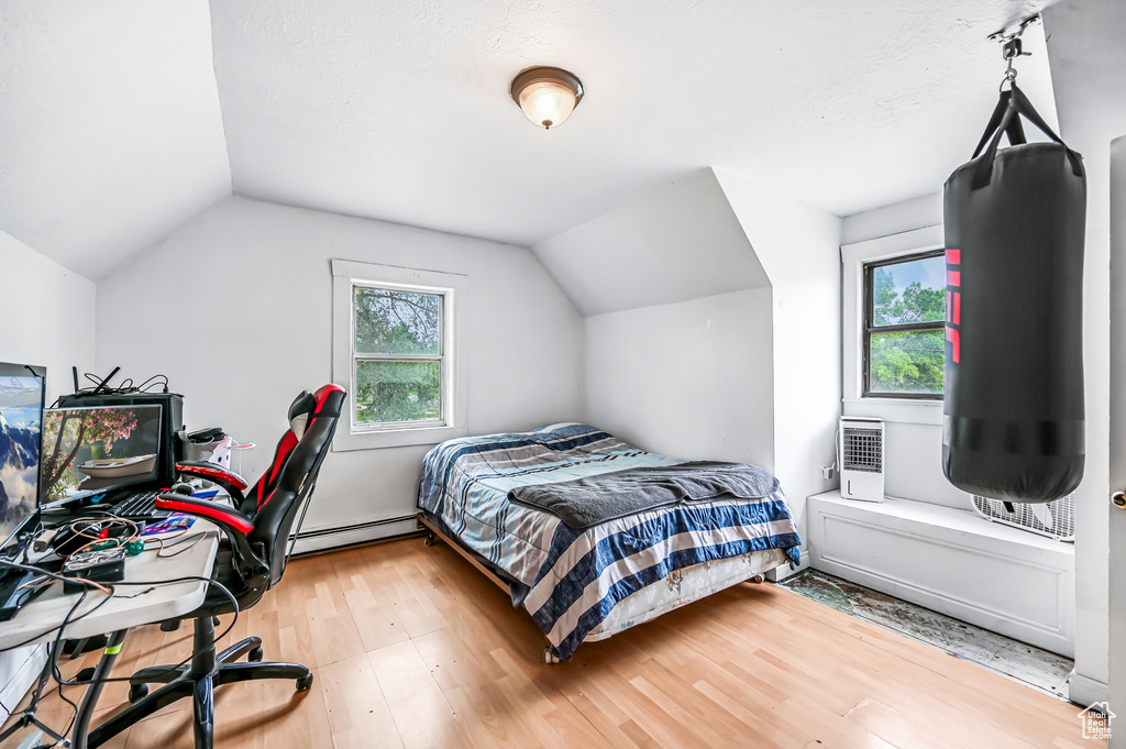 Bedroom with lofted ceiling, wood finished floors, and a baseboard heating unit