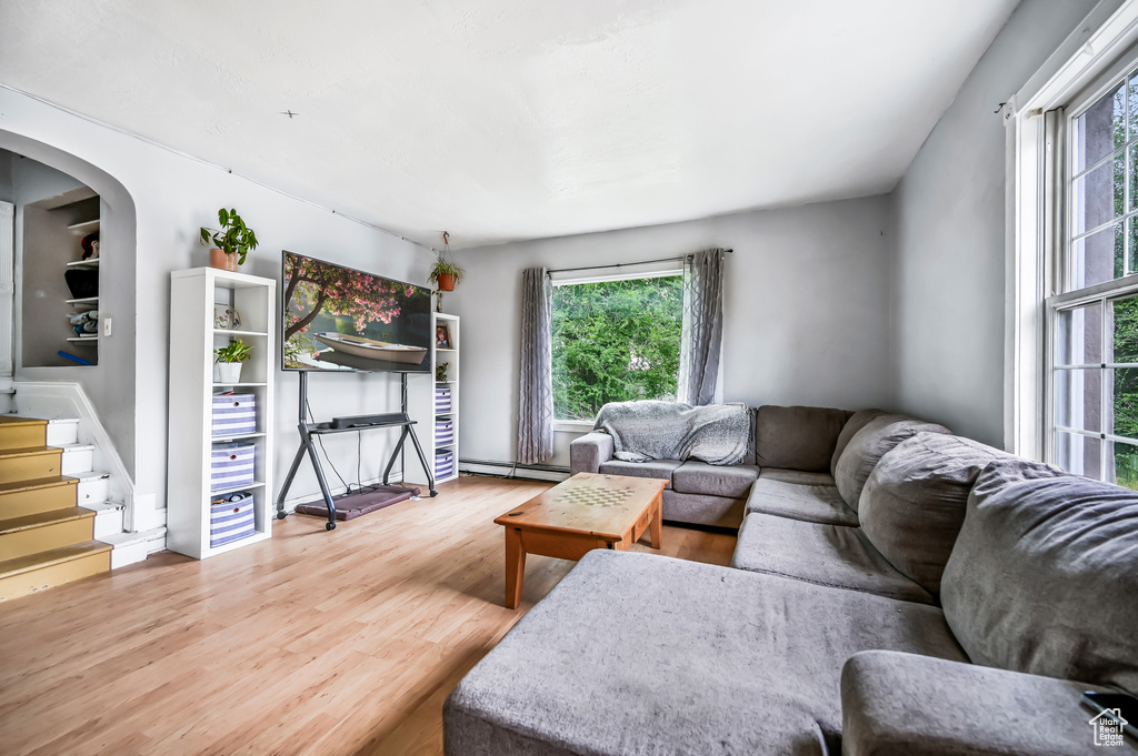 Living room featuring a baseboard heating unit, wood finished floors, plenty of natural light, and stairs