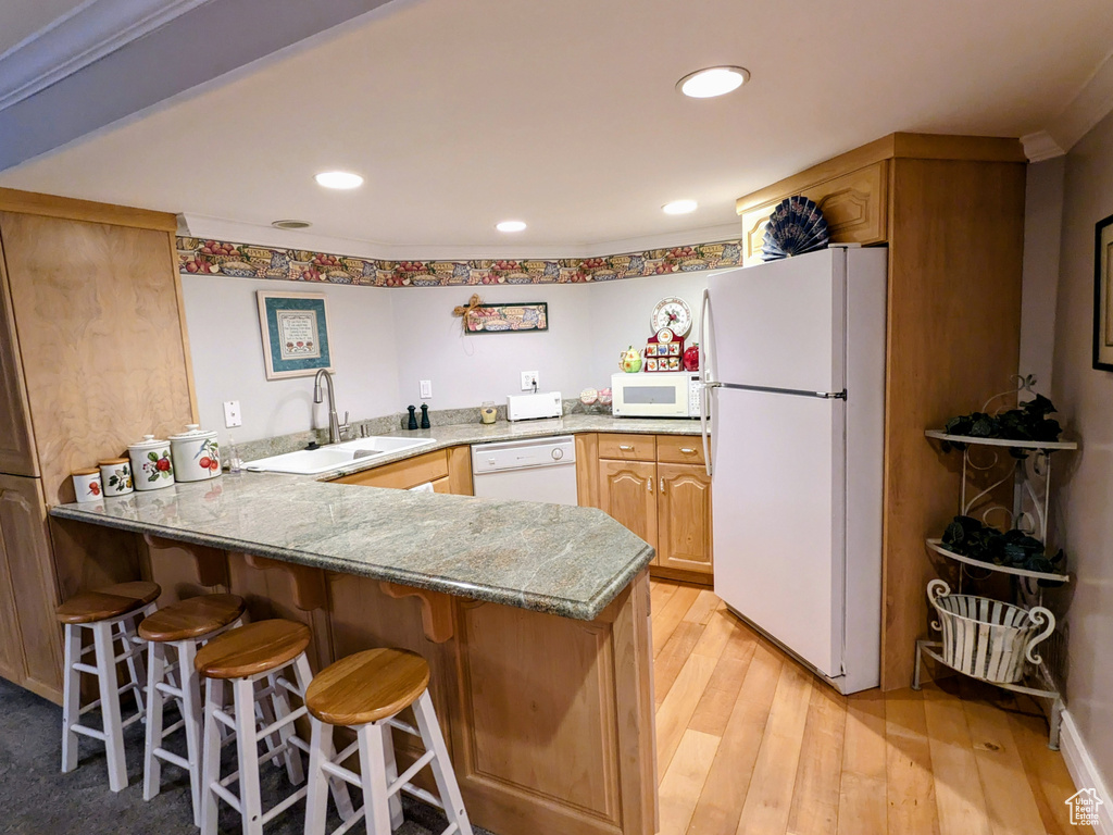 Kitchen with white appliances, a sink, a peninsula, light wood-type flooring, and a breakfast bar