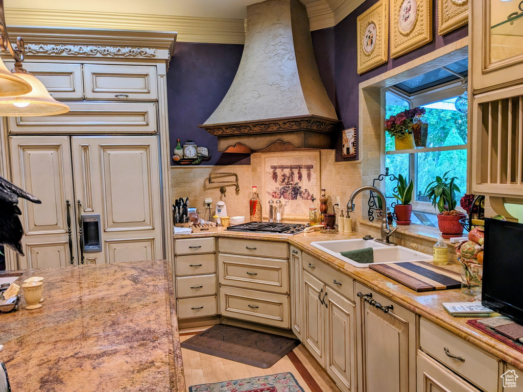 Kitchen with premium range hood, a sink, cream cabinetry, stainless steel gas cooktop, and tasteful backsplash