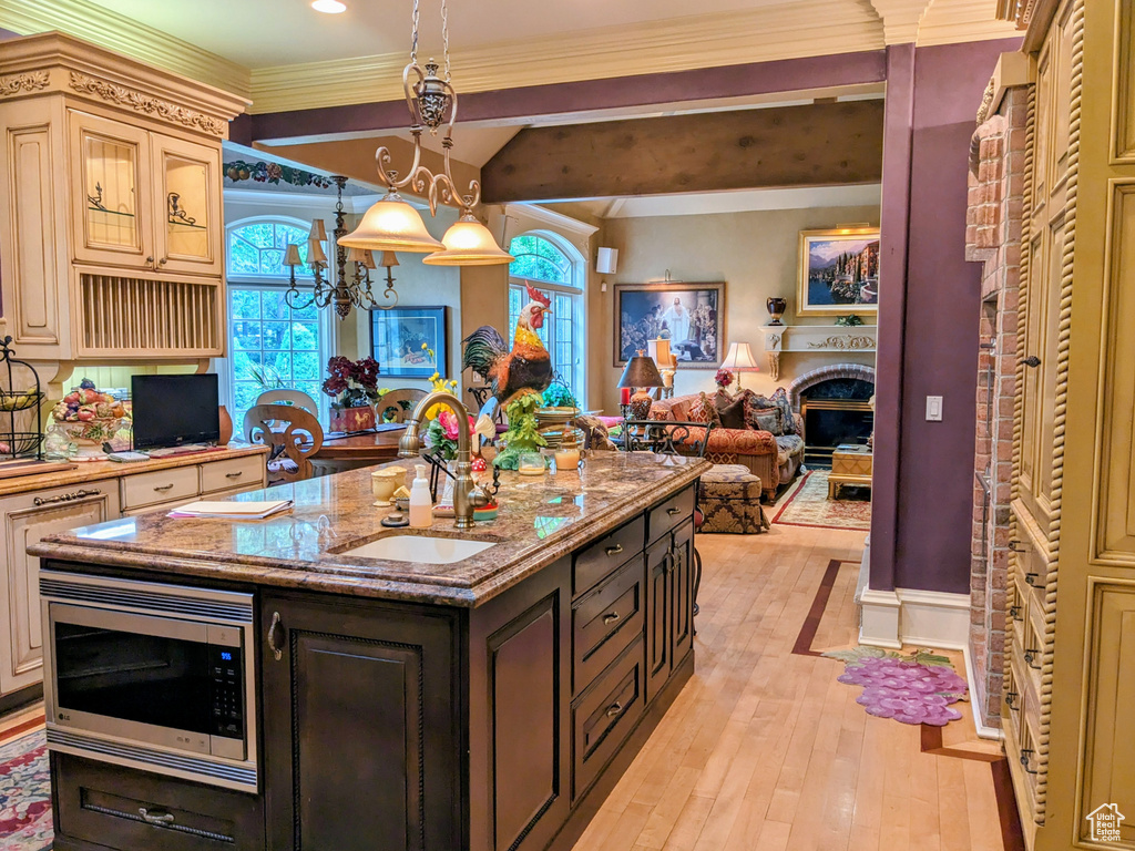 Kitchen with stainless steel microwave, a sink, open floor plan, light wood-type flooring, and cream cabinetry