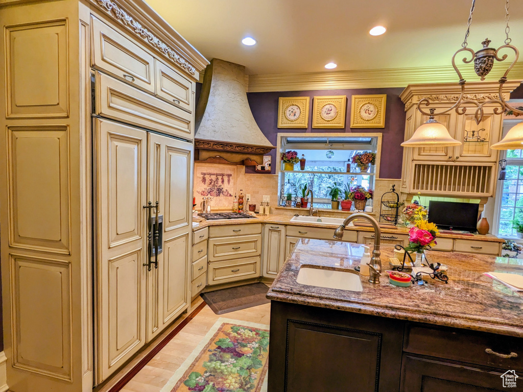 Kitchen featuring cream cabinetry, premium range hood, a sink, stainless steel gas stovetop, and backsplash