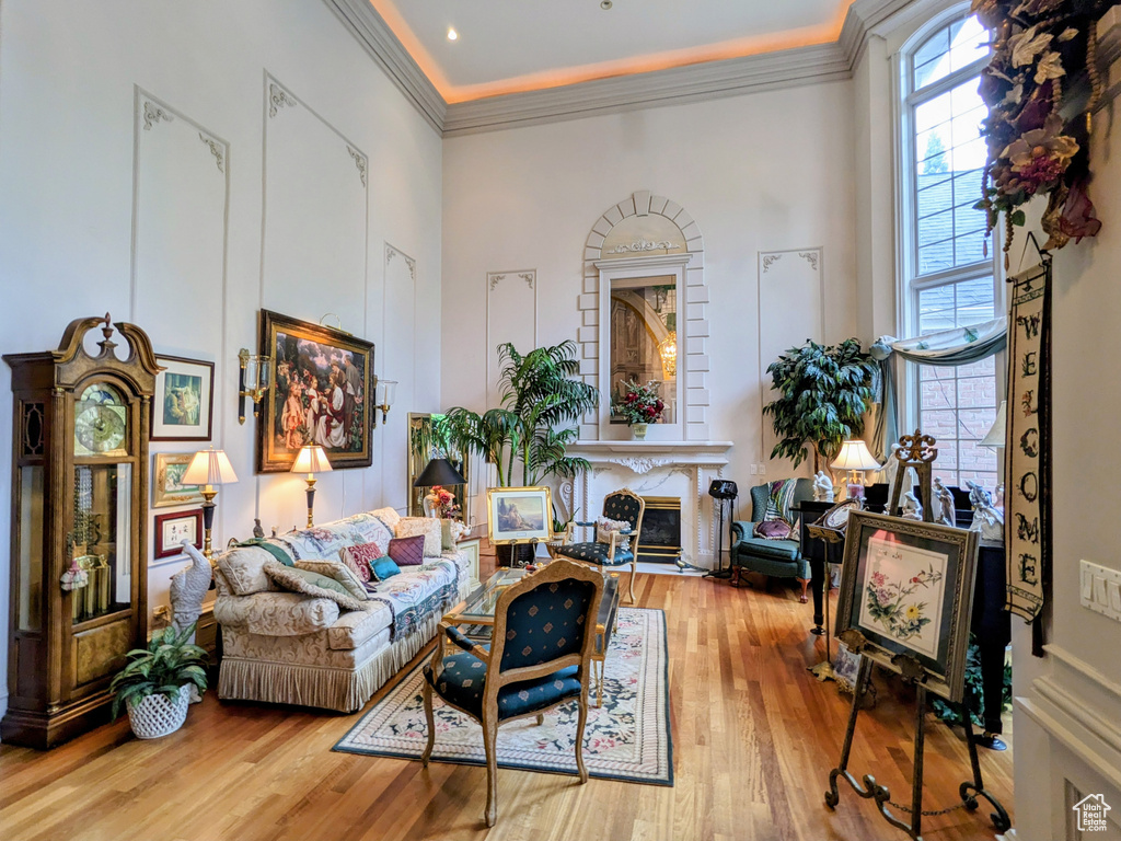 Living room featuring a premium fireplace, crown molding, wood finished floors, and a towering ceiling