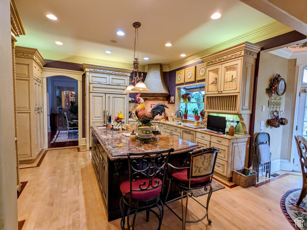 Kitchen featuring custom range hood, ornamental molding, light wood-style floors, cream cabinets, and a kitchen island