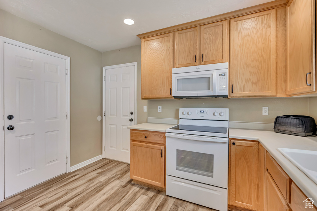 Kitchen with white appliances, light wood-type flooring, light countertops, light brown cabinets, and recessed lighting