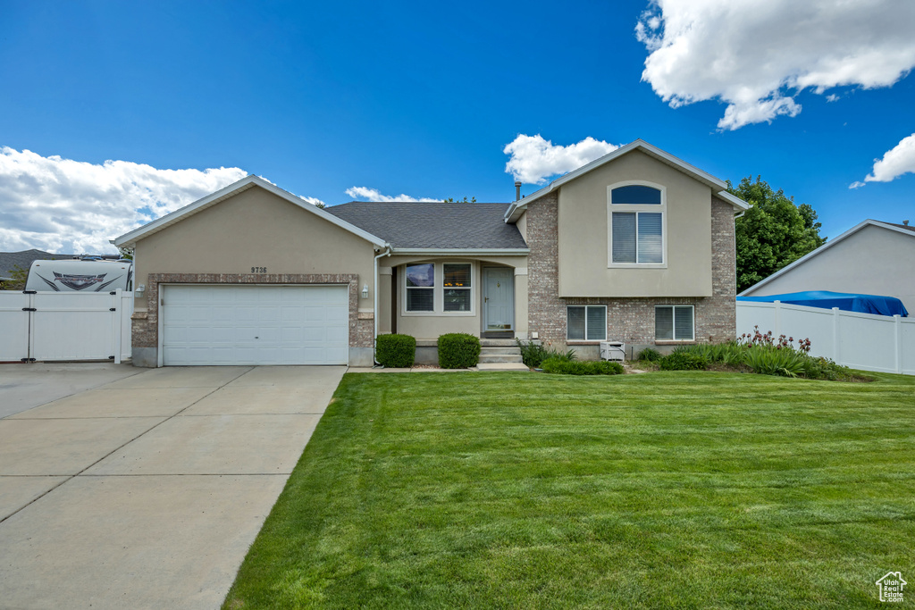 Tri-level home with stucco siding, a garage, concrete driveway, and a gate