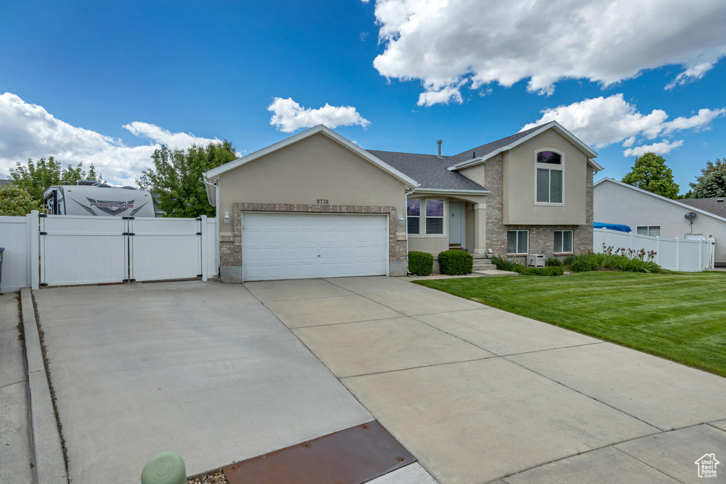 Split level home featuring a gate, stucco siding, an attached garage, and concrete driveway