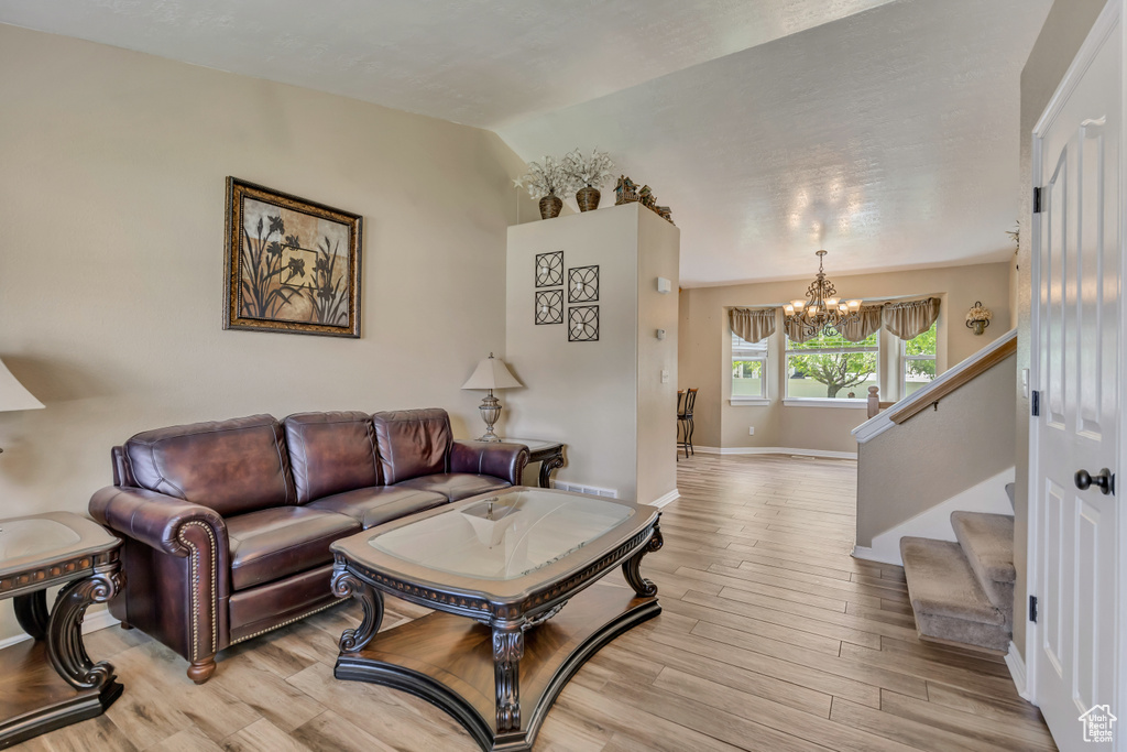 Living room featuring a chandelier, light wood-style flooring, lofted ceiling, baseboards, and stairs