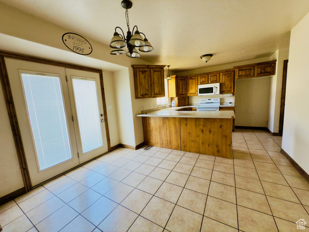 Kitchen featuring white appliances, a peninsula, light countertops, light tile patterned flooring, and a chandelier