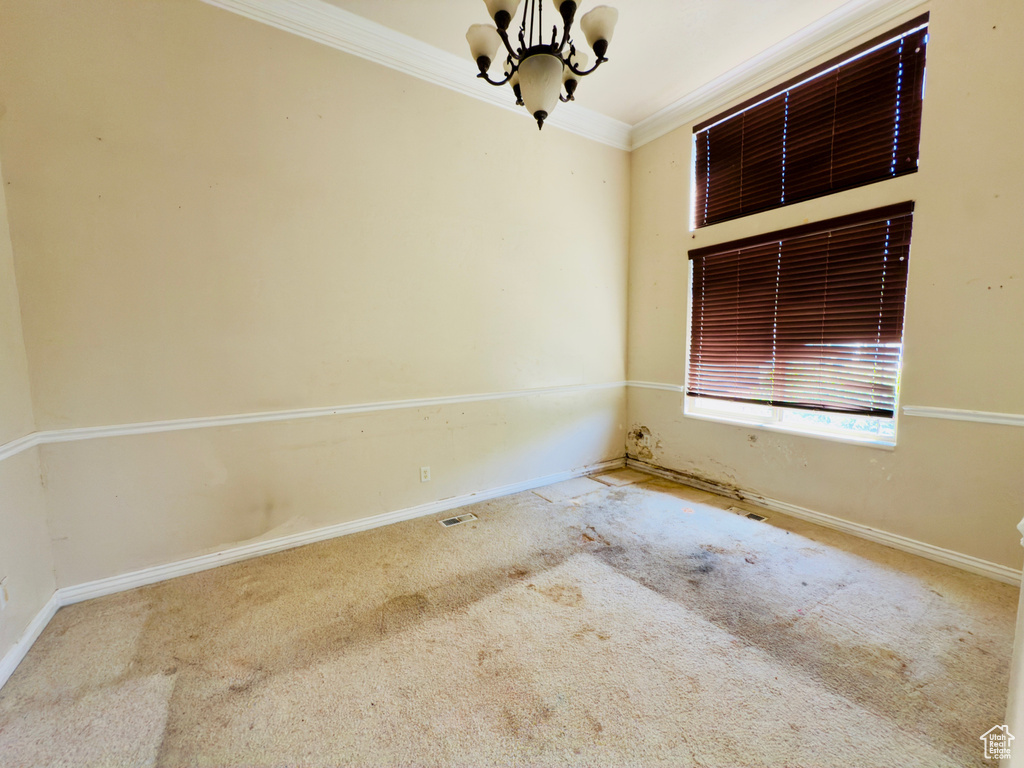 Carpeted spare room featuring a chandelier, ornamental molding, and baseboards