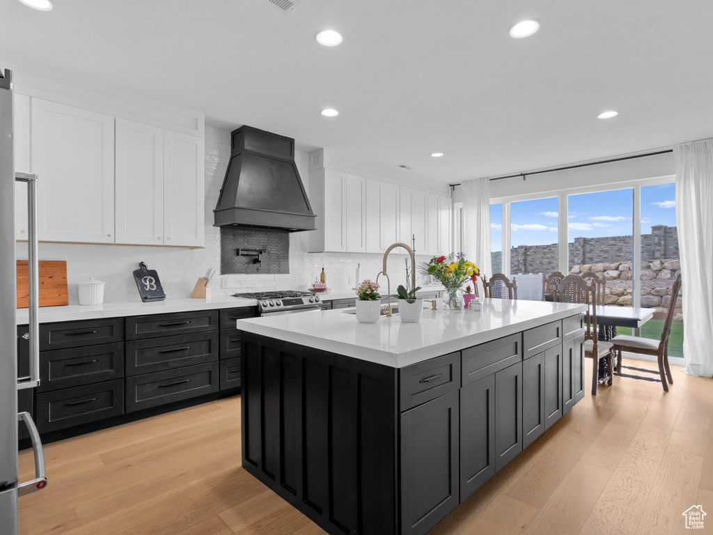 Kitchen with premium range hood, white cabinetry, light countertops, decorative backsplash, and light wood finished floors