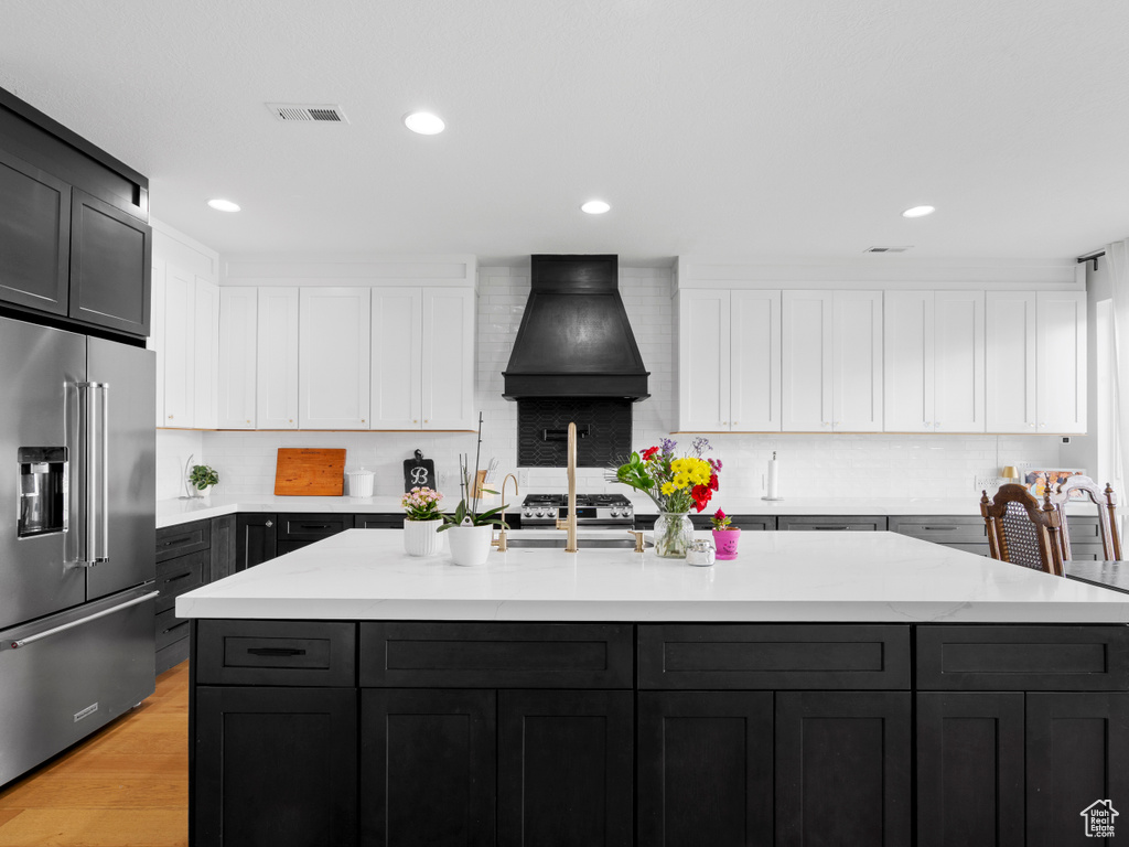 Kitchen with high end refrigerator, custom exhaust hood, white cabinets, backsplash, and recessed lighting
