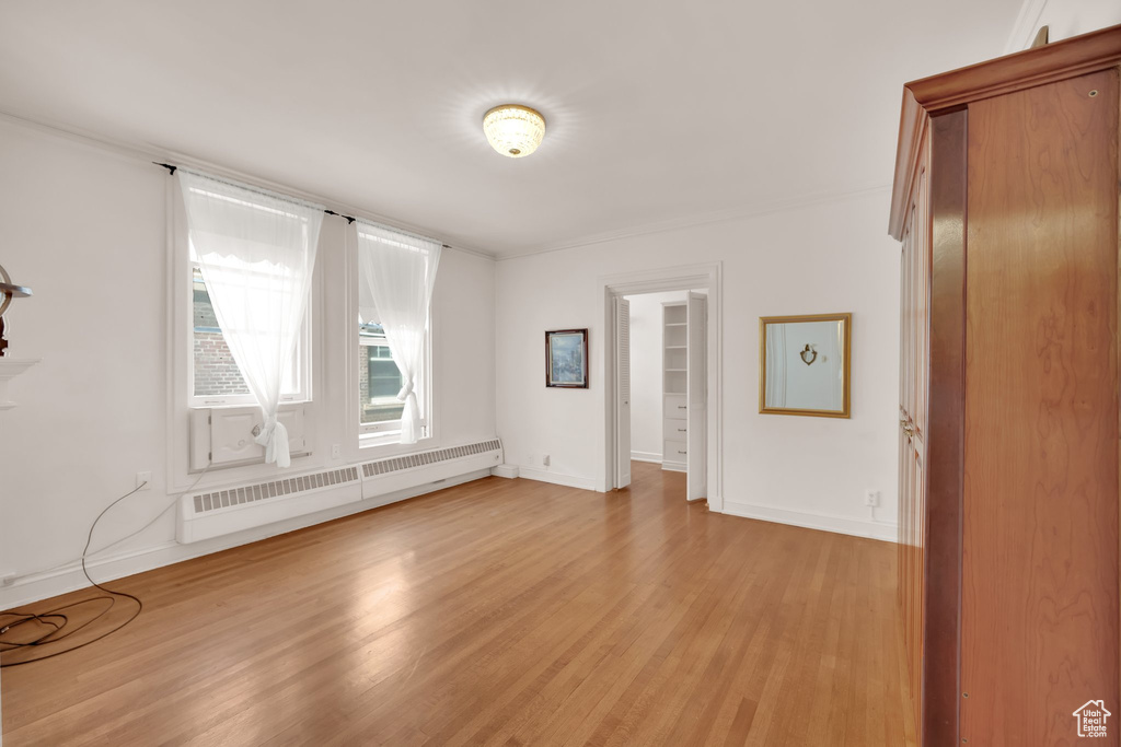 Unfurnished room with a baseboard heating unit, light wood-style floors, and baseboards