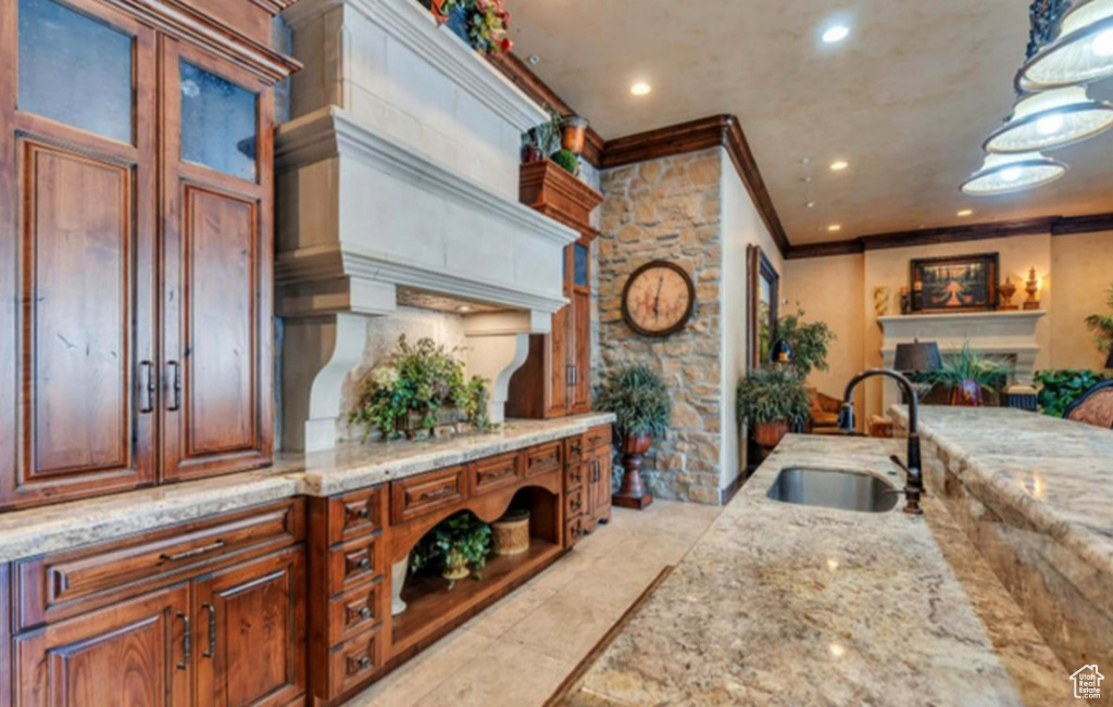 Kitchen with a sink, ornamental molding, a fireplace, light stone counters, and recessed lighting