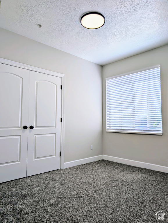 Unfurnished bedroom featuring dark colored carpet, baseboards, a closet, and a textured ceiling