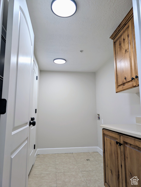 Laundry room featuring a textured ceiling, baseboards, and cabinet space