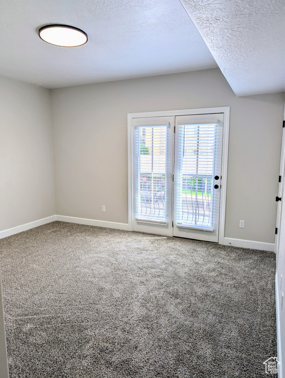 Carpeted empty room with a textured ceiling and baseboards