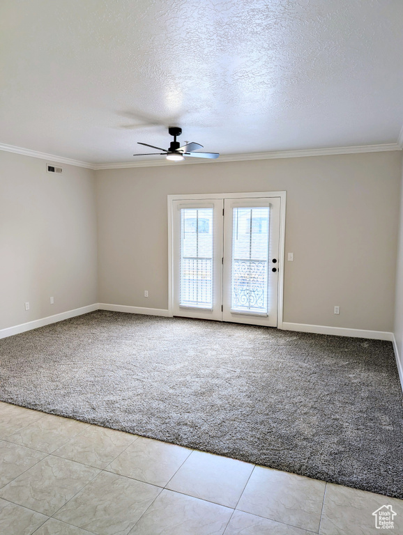 Carpeted spare room featuring crown molding, ceiling fan, baseboards, a textured ceiling, and tile patterned floors