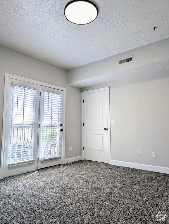 Empty room with a textured ceiling, carpet floors, baseboards, and fire sprinkler in ceiling