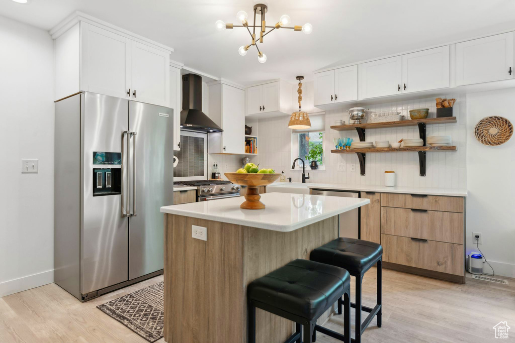 Kitchen featuring appliances with stainless steel finishes, wall chimney exhaust hood, open shelves, decorative backsplash, and light wood finished floors