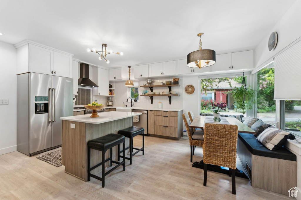 Kitchen with appliances with stainless steel finishes, open shelves, wall chimney range hood, light countertops, and light wood-style floors