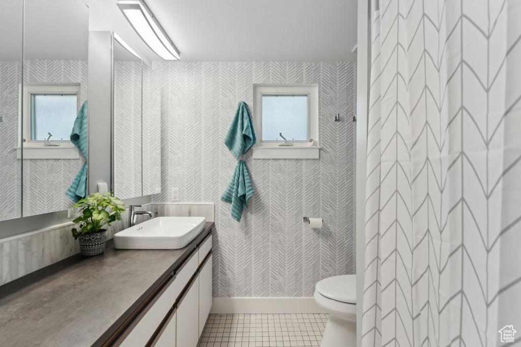 Full bathroom with wallpapered walls, toilet, tile patterned flooring, healthy amount of natural light, and vanity