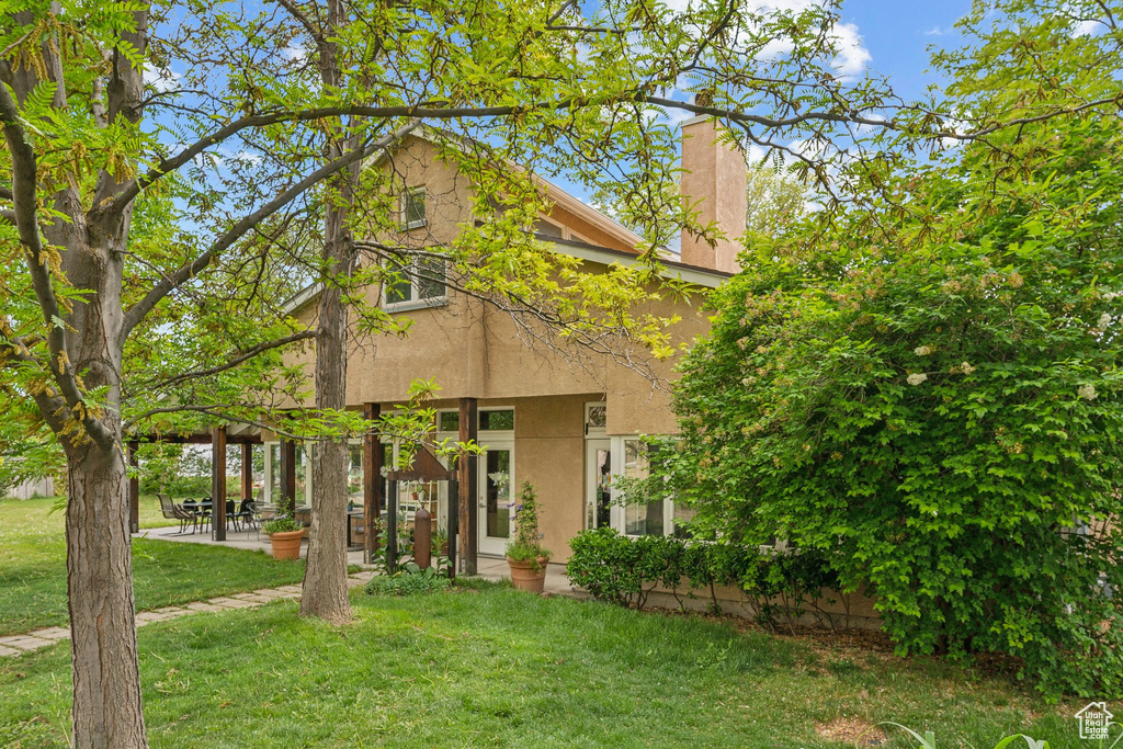 View of front of home featuring a front yard, stucco siding, a patio, and a chimney