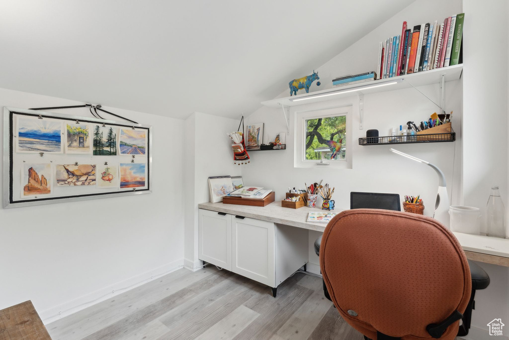 Office featuring light wood finished floors, vaulted ceiling, built in desk, and baseboards