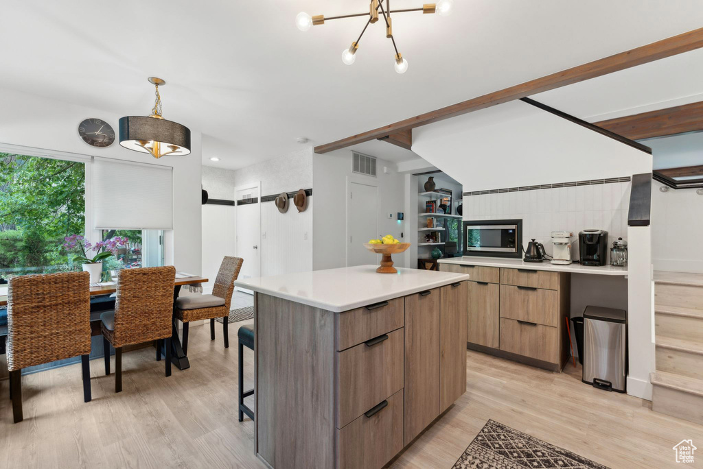 Kitchen featuring modern cabinets, stainless steel microwave, a kitchen island, light wood-style floors, and light countertops