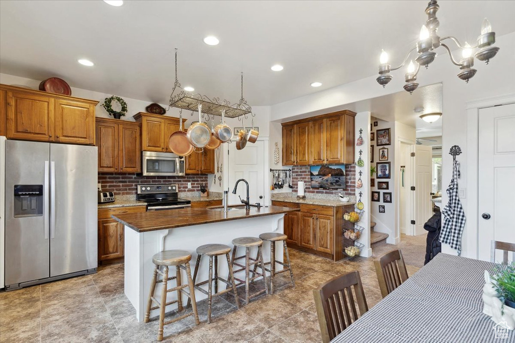 Kitchen featuring stainless steel appliances, a sink, brown cabinetry, backsplash, and a center island with sink
