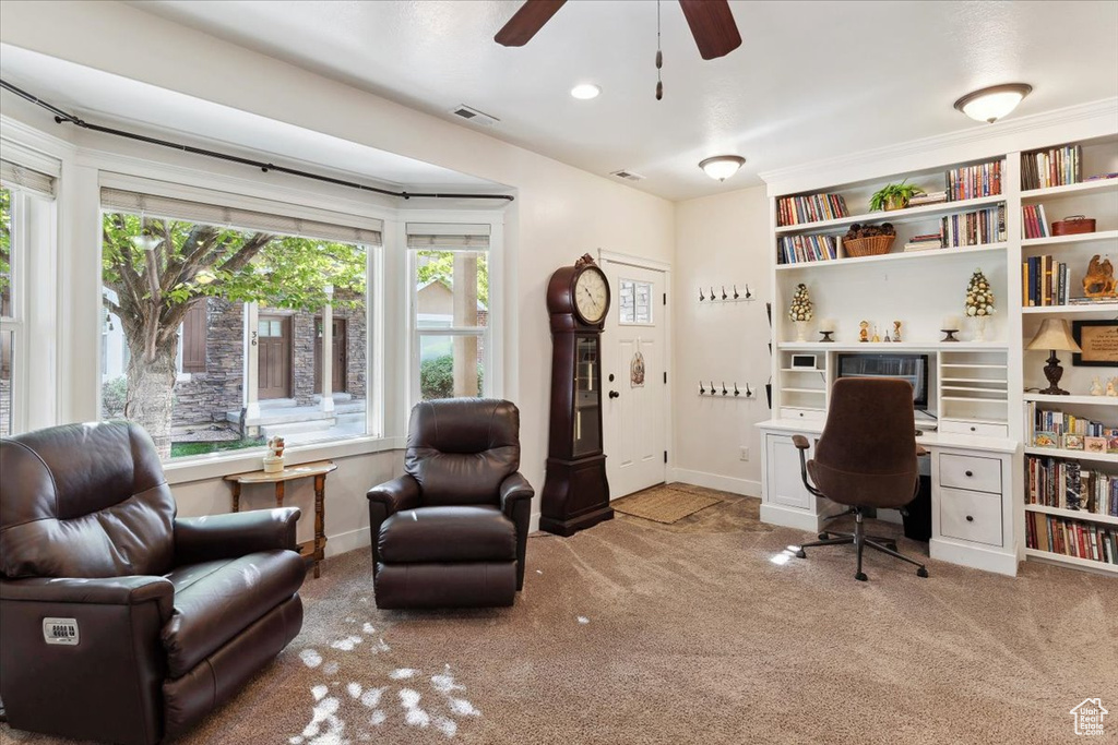Carpeted home office featuring ceiling fan, baseboards, and built in desk