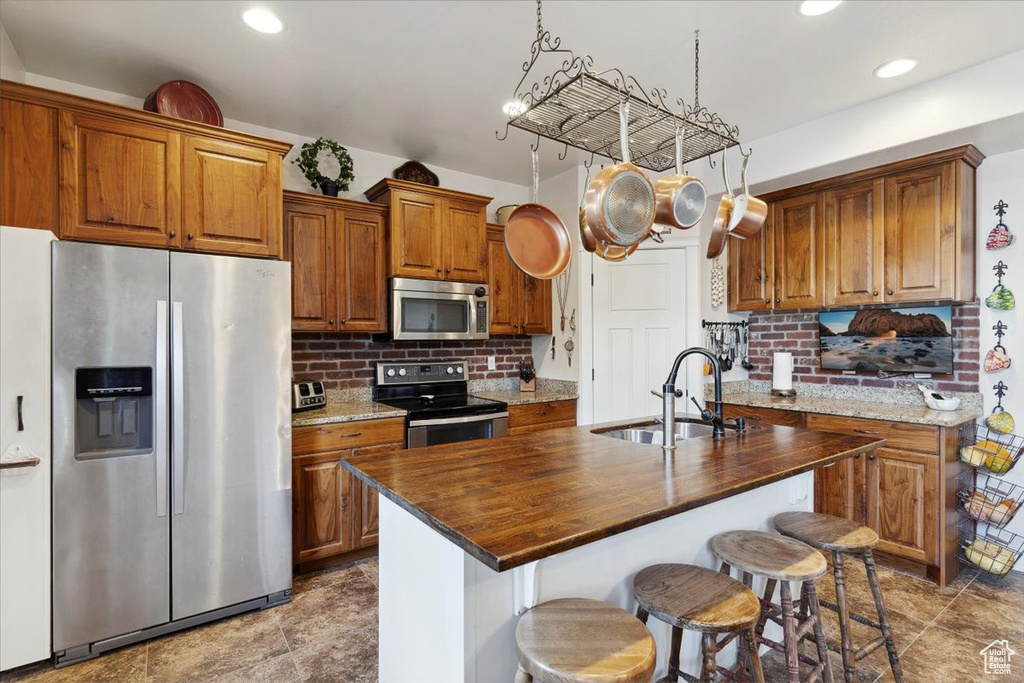 Kitchen featuring stainless steel appliances, a sink, brown cabinetry, decorative backsplash, and recessed lighting