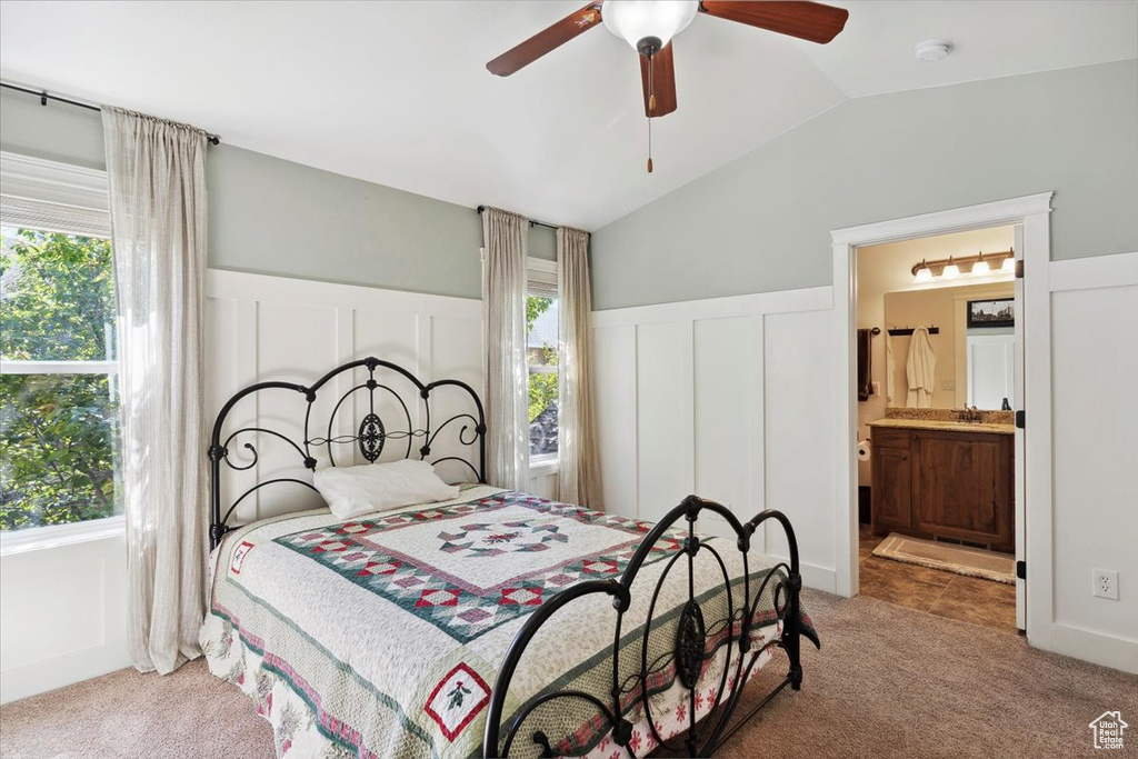 Carpeted bedroom with lofted ceiling, a wainscoted wall, a decorative wall, ensuite bath, and a ceiling fan