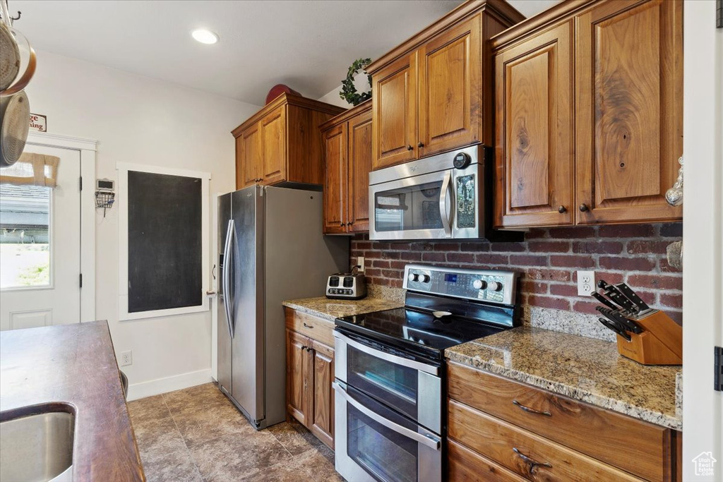 Kitchen with appliances with stainless steel finishes, brown cabinets, light stone countertops, tasteful backsplash, and recessed lighting