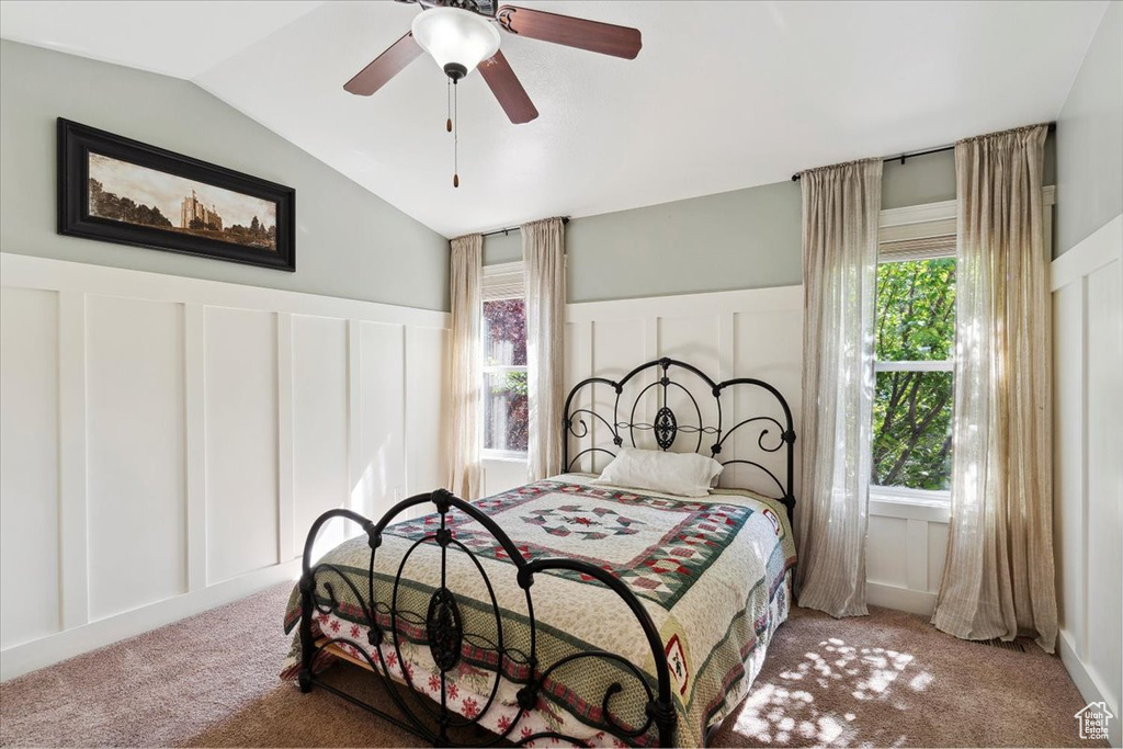 Bedroom featuring a decorative wall, carpet flooring, lofted ceiling, a wainscoted wall, and ceiling fan