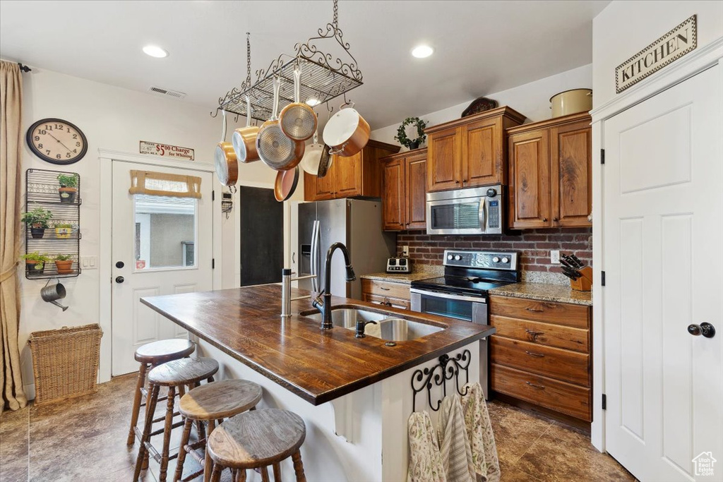 Kitchen featuring stainless steel appliances, a sink, brown cabinets, decorative backsplash, and an island with sink