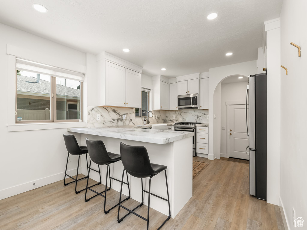Kitchen featuring stainless steel appliances, a peninsula, a breakfast bar area, white cabinetry, and decorative backsplash