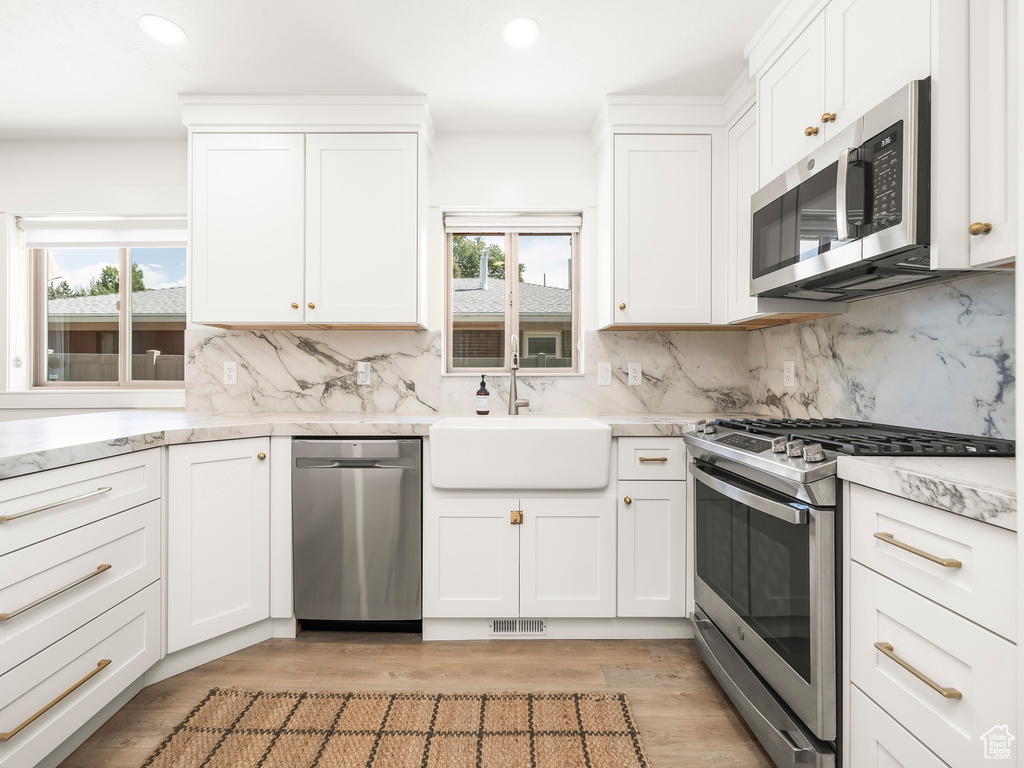 Kitchen featuring appliances with stainless steel finishes, a sink, backsplash, recessed lighting, and white cabinetry