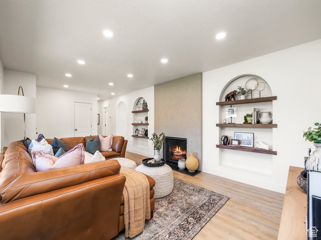 Living room featuring light wood-style flooring, recessed lighting, a large fireplace, built in shelves, and baseboards