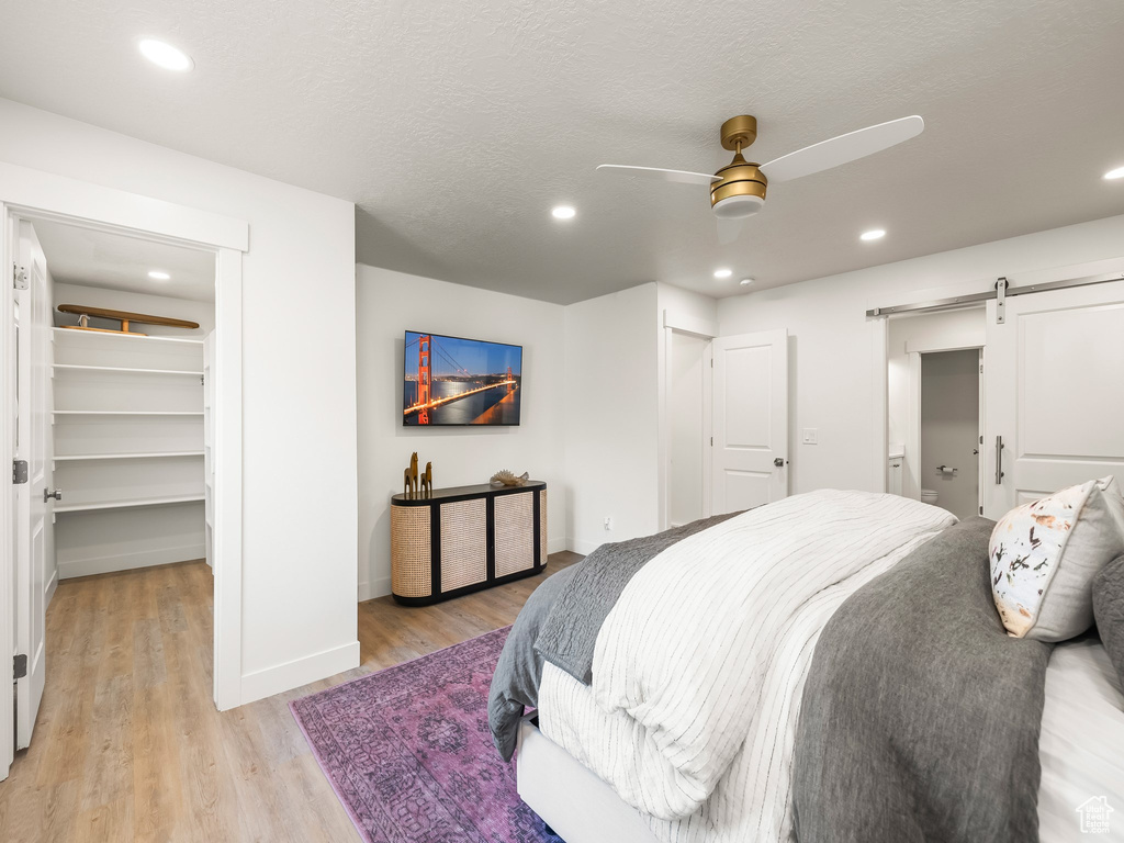 Bedroom featuring a barn door, light wood-style flooring, a spacious closet, recessed lighting, and a closet