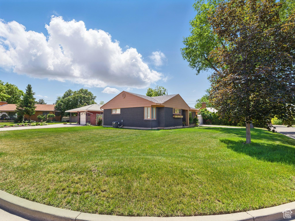 View of side of property with driveway, a lawn, brick siding, and an attached garage