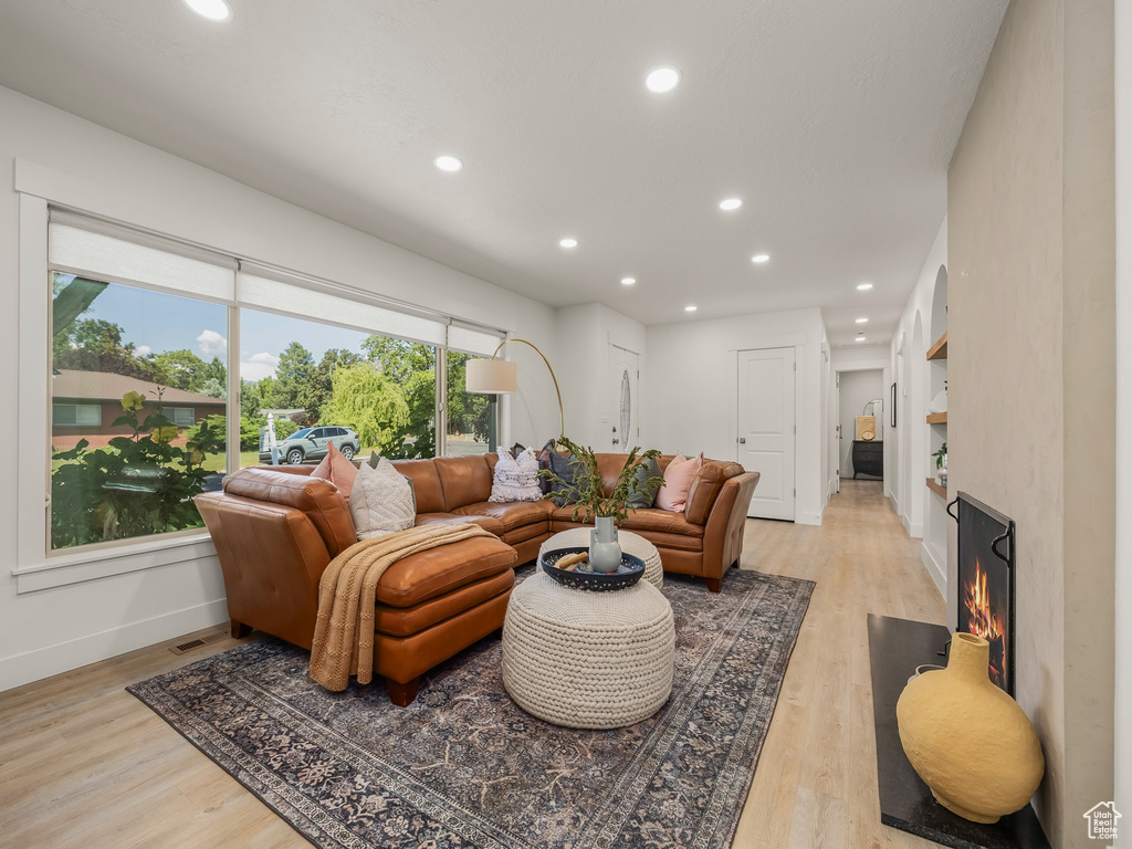 Living room with baseboards, recessed lighting, light wood finished floors, and a warm lit fireplace